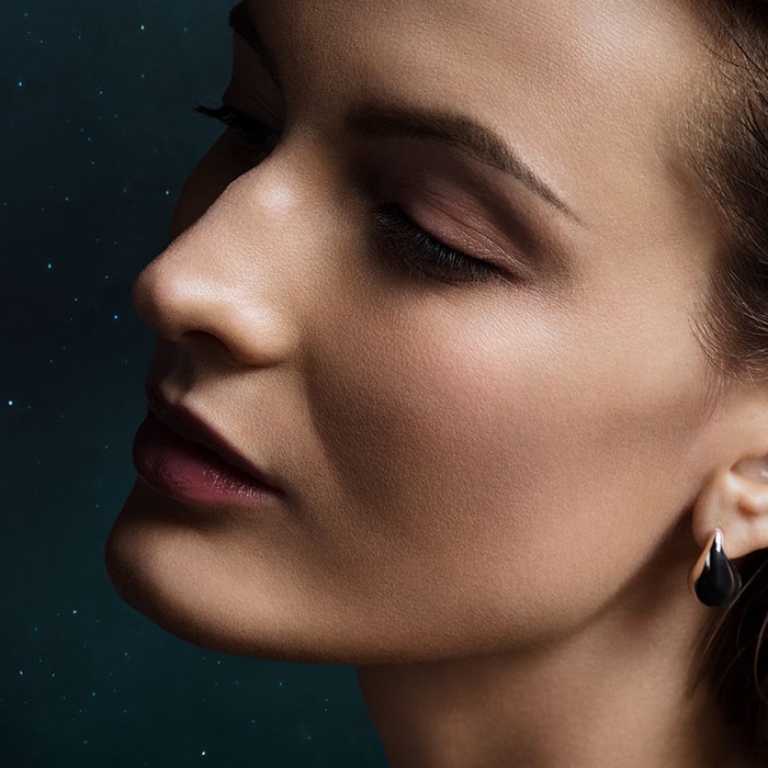 Close up of a womans face with closed eyes and slightly tilted head backwards in dark shadow.