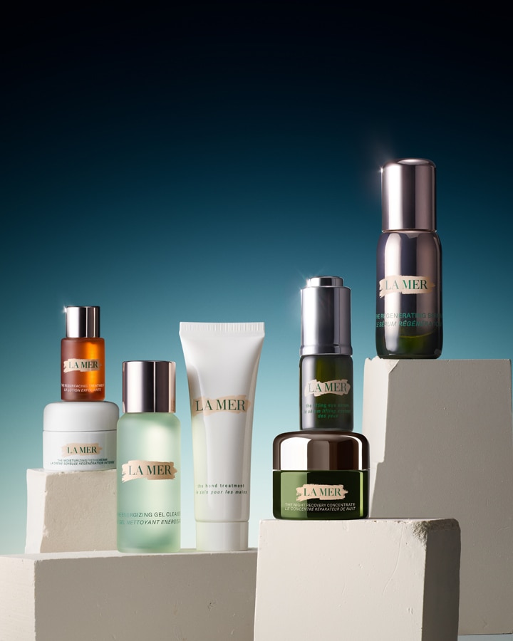 A variety of La Mer skincare products are displayed on white geometric blocks against a gradient blue background.